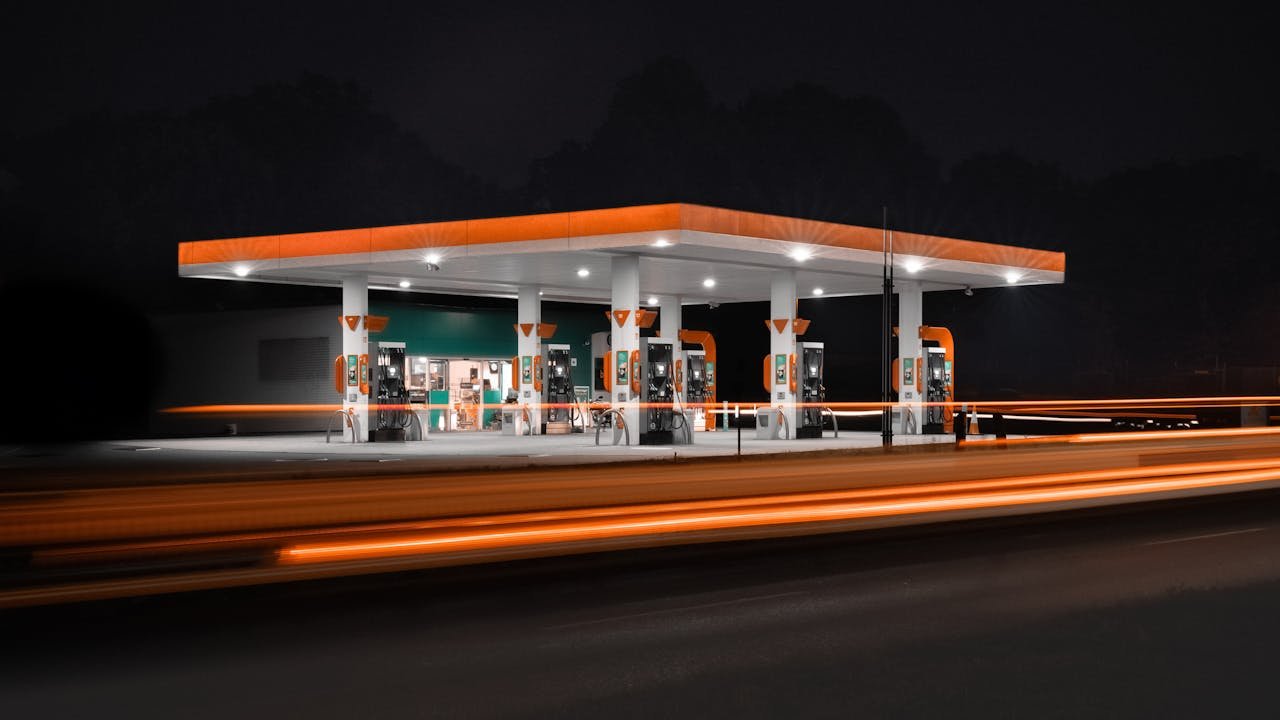 Gas station illuminated at night with motion blur from passing vehicles.